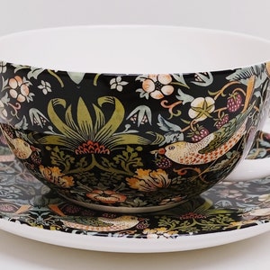 May include: A black and white teacup and saucer set with a floral and bird pattern. The cup is large and has a wide rim. The saucer is round and has a matching pattern.