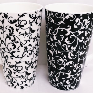 Può includere: Due grandi tazze in ceramica con motivi floreali in bianco e nero. Le tazze hanno una forma conica e un manico.