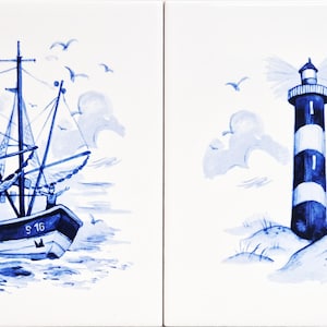 May include: Two square ceramic tiles with blue and white nautical designs. One tile depicts a sailboat with the number "S 16" on the hull. The other tile shows a lighthouse with blue and white stripes, with birds and clouds.