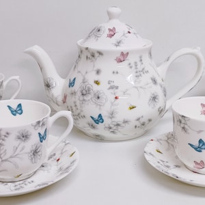 May include: A white porcelain tea set featuring a butterfly and floral design. The set includes a teapot, four cups, and four saucers.