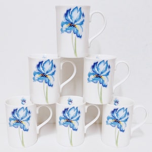 May include: Set of six white ceramic mugs with blue watercolour iris flower designs. The mugs have a handle on the right side.