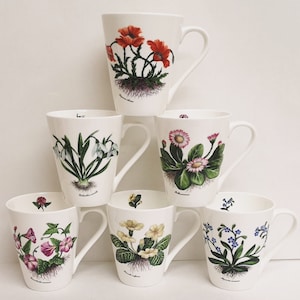 May include: Set of six white ceramic mugs with floral designs. Each mug features a different flower, including a poppy, snowdrop, daisy, primrose, forget-me-not, and a pink flower.