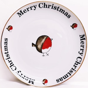 May include: White ceramic plate with a gold rim. The plate features a black and red robin illustration in the centre and the words "Merry Christmas" repeated around the edge.