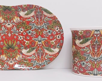 May include: A red and green ceramic teacup and saucer set with a floral pattern featuring birds. The pattern is inspired by William Morris's Strawberry Thief design.
