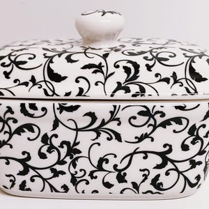 May include: A white ceramic butter dish with a black and white floral pattern. The lid has a knob on top.