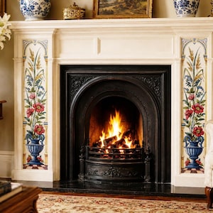 May include: A white fireplace mantel featuring decorative vertical tile panels on each side, each displaying a blue urn filled with red flowers and green foliage. The central black cast iron firebox contains a burning fire with orange flames.