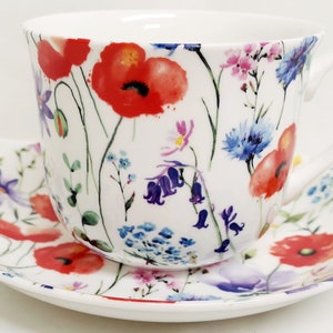 Peut inclure: Une tasse à thé et une soucoupe blanches avec un motif floral représentant des coquelicots rouges, des campanules et d'autres fleurs sauvages.