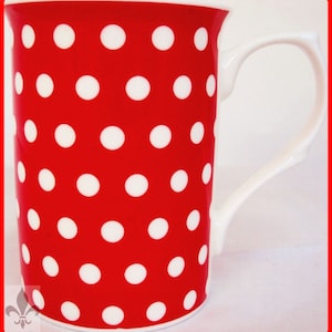 Könnte beinhalten: Eine rote Keramiktasse mit einem weißen Tupfenmuster. Die Tasse hat einen weißen Henkel.