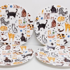 May include: Set of four white ceramic dinner plates with a repeating pattern of colorful cats and paw prints.