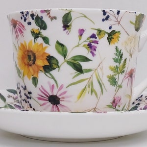 Peut inclure: Service à thé en céramique blanche. La tasse et la soucoupe sont décorées d'un motif floral coloré avec des tournesols, des échinacées pourpres et du feuillage vert. La tasse a une anse incurvée.