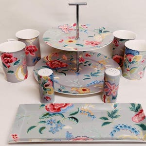 May include: A grey floral patterned tea set including a two-tiered cake stand, mugs, salt and pepper shakers, and a rectangular serving platter. The set features a floral design in red, pink, blue, and yellow.