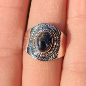 May include: A silver ring featuring a black and gold oval gemstone set within a decorative silver bezel. The ring has a textured band.