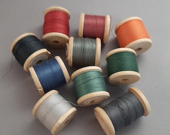 Può includere: Una collezione di rocchetti di filo colorati. I rocchetti di legno sono riempiti di filo in vari colori, tra cui rosso, arancione, verde, blu e grigio. I rocchetti sono disposti su una superficie grigia.