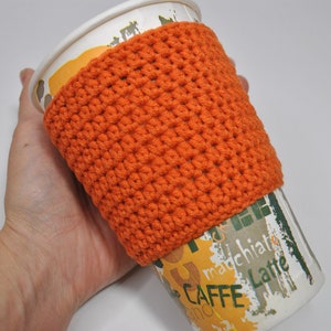 May include: Orange crocheted coffee cup cozy. The cozy is made with a simple stitch pattern and is a great way to keep your hands warm while enjoying your favorite beverage.