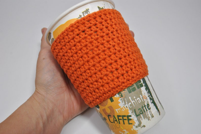 May include: Orange crocheted coffee cup cozy. The cozy is made with a simple stitch pattern and is a great way to keep your hands warm while enjoying your favorite beverage.