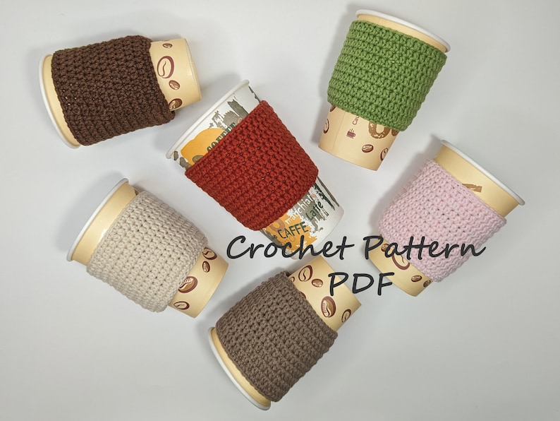 May include: Six crocheted coffee cup cozies in various colors, including brown, red, green, beige, pink, and gray. The cozies are on top of disposable coffee cups with a coffee bean pattern. The text "Crochet Pattern PDF" is written in black on a white background.