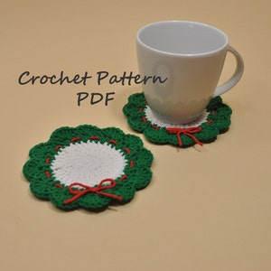 Puede incluir: Dos posavasos de ganchillo hechos a mano con diseño de corona. Los posavasos tienen un centro blanco, bordes festoneados verdes y detalles rojos. Un posavasos tiene una taza blanca encima. El texto "Crochet Pattern PDF" está en la parte superior izquierda.