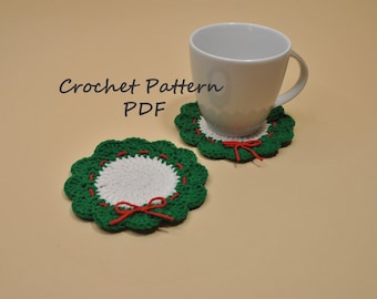 May include: Two handmade crochet coasters in a wreath design. The coasters feature a white center, green scalloped edges, and red accents. One coaster has a white mug on top. The text "Crochet Pattern PDF" is in the upper left.