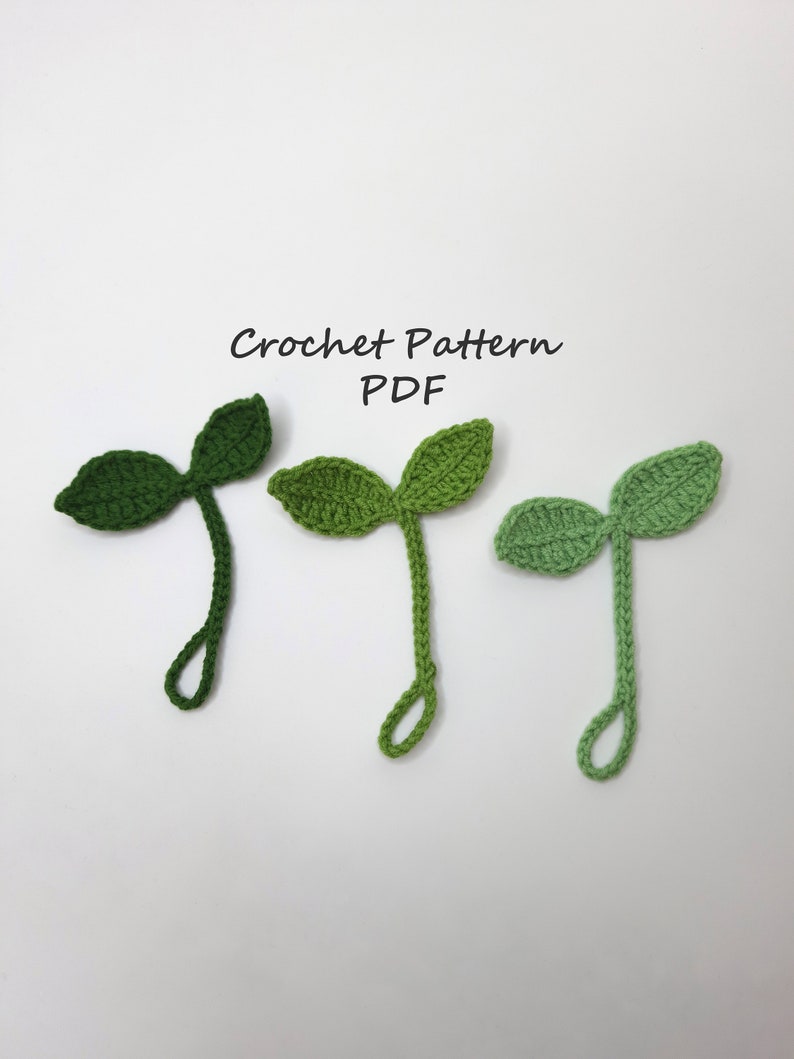May include: Three crocheted leaf shapes in varying shades of green, arranged on a white background. The leaves have a detailed texture and are connected to a stem with a loop at the end. The text "Crochet Pattern PDF" is above the leaves.