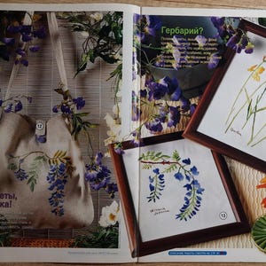 Puede incluir: Una página de revista con un bolso de mano de lona y arte botánico enmarcado. El bolso de mano muestra un diseño floral azul y verde, con el texto "¡Verano, flores, romance!" El arte enmarcado presenta pinturas de flores a la acuarela.