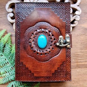 May include: A brown leather journal with a turquoise stone inlay and a brass clasp. The journal has intricate embossed designs on the cover.