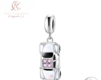 May include: A silver car charm with white enamel detailing, black windows, and pink gemstones. The charm is suspended from a silver bail. The charm is from The Charming Keepsake Co.