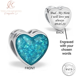 May include: A heart-shaped charm with a metallic silver frame and a shimmering teal blue front. The back is engraved with the text: Dad, My Hero I will love you always 09.05.23. A circular stamp indicates 925 real sterling silver.