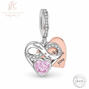May include: A silver charm featuring an infinity symbol encrusted with clear stones, inscribed with the words Daughter in law. A pink heart-shaped stone sits below the infinity symbol, and a rose gold heart charm is engraved with the text love you.