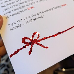 May include: A white card with red glitter accents. The card features a red glitter bow and the text "If you look for it, I've got a sneaky feeling love, actually... is all around."