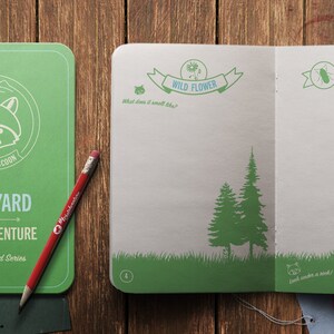 Peut inclure: Un carnet vert avec une illustration de raton laveur et le texte "Backyard Sketch Venture Neighborhood Series". Le carnet est ouvert &agrave; une page avec une illustration verte et blanche d'une fleur sauvage et d'un pin.