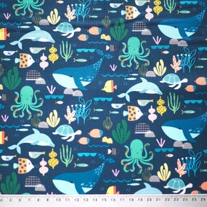 Könnte beinhalten: Ein blauer Stoff mit einem sich wiederholenden Muster aus bunten Meeresbewohnern, darunter Wale, Delfine, Kraken, Schildkröten und Fische. Der Hintergrund ist dunkelblau.