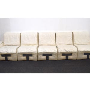 May include: A white modular sofa with five sections, each with a black strap across the front. The sofa is made of a soft, white fabric and has a simple, modern design.