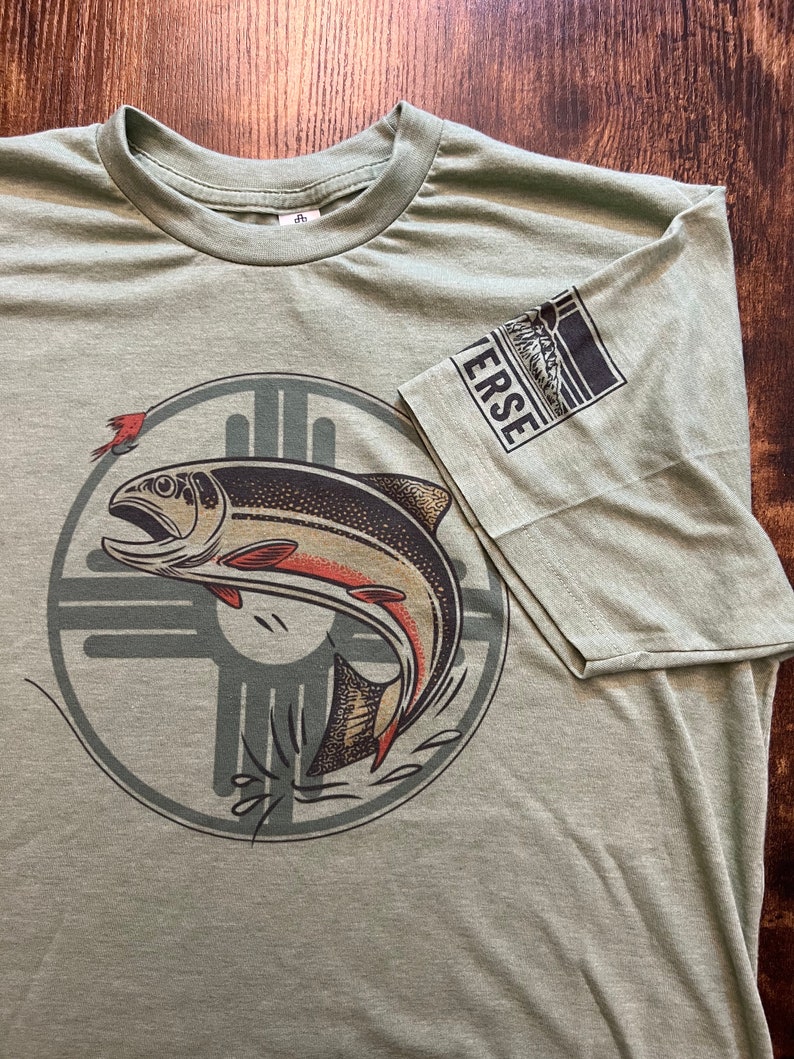 May include: A green t-shirt with a graphic of a fish jumping out of the water. The fish is surrounded by a circle with a stylized design. The text "VERSE" is on the sleeve of the shirt.