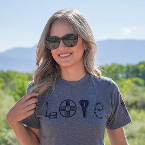 May include: A woman wearing sunglasses and a heather grey t-shirt with a graphic design of the word "LOVE" made up of bicycle parts. The "O" is a bicycle wheel with a symbol in the center, the "V" is a bicycle seat, and the "E" is a bicycle chain.