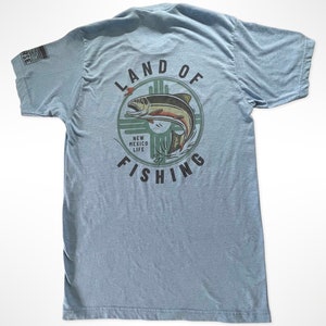 May include: A light blue t-shirt with a graphic of a fish jumping out of the water. The graphic is surrounded by a circle with the text "Land of Fishing" and "New Mexico Life".