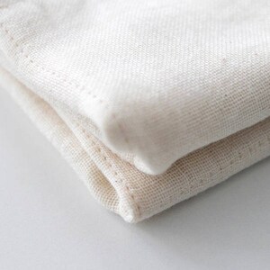 May include: A close-up of a folded white cotton fabric. The fabric is soft and has a slightly textured surface.