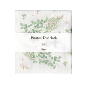 May include: A white dishcloth with a floral print of green leaves and pink flowers. The dishcloth has a label that says "Printed Dishcloth".