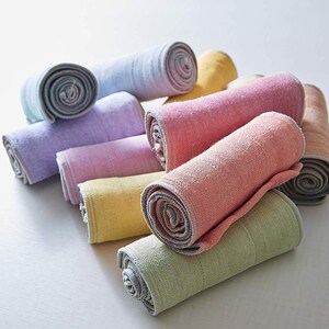 May include: A collection of rolled up towels in various pastel colors, including light blue, lavender, pink, yellow, and green. The towels are made of a soft, textured fabric and have a subtle sheen.