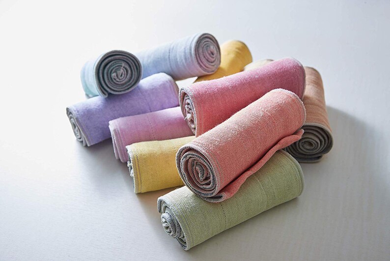May include: A collection of rolled up towels in various pastel colors, including light blue, lavender, pink, yellow, and green. The towels are made of a soft, textured fabric and have a subtle sheen.