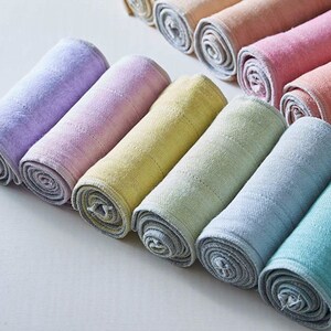 May include: A set of ten rolled up, colorful, cotton washcloths. The washcloths are in shades of purple, pink, yellow, green, and blue.