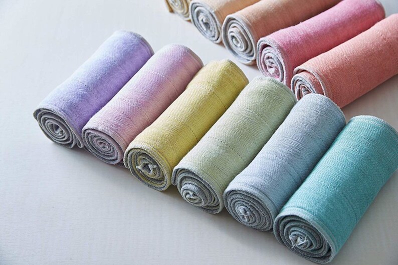 May include: A set of ten rolled up, colorful, cotton washcloths. The washcloths are in shades of purple, pink, yellow, green, and blue.