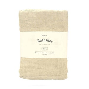 Puede incluir: Una alfombra de baño beige con una etiqueta blanca que dice "Bathmat" en negro. La etiqueta también incluye el texto japonés "バスマット" y "リネン" en negro. La etiqueta también incluye el texto "Maruyama Fiber Industry Co., Ltd. since 1930" en negro.
