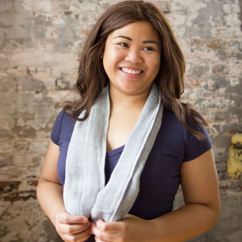 May include: A woman with long brown hair is wearing a gray scarf and a dark blue shirt. She is smiling and looking at the camera.