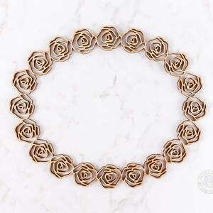 May include: An overhead shot showcases a circular arrangement of wooden rose cutouts. The roses are a warm, natural wood tone, set against a white and gray marble-patterned background. The design creates a decorative border.