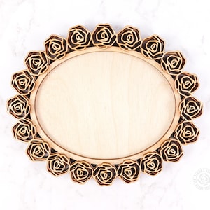 May include: Oval wooden plaque with a light wood center and a border of layered, laser-cut roses in a darker wood tone. The roses encircle the oval, creating a decorative frame. The background is a white marble-like surface.