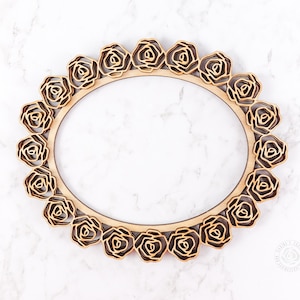 May include: A wooden frame with a decorative design of roses around the perimeter. The frame is light brown and has a natural wood finish.