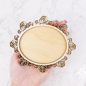 Puede incluir: Un marco redondo de madera con un dise&ntilde;o decorativo de rosas. El marco est&aacute; en blanco y listo para personalizar.