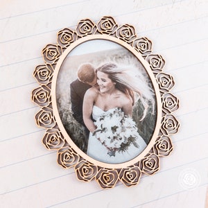May include: A wooden picture frame with a decorative rose design. The frame is oval shaped and has a photo of a bride and groom inside.