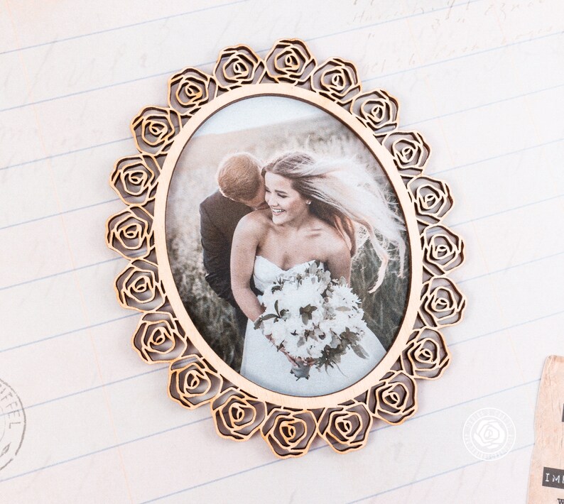 May include: A wooden picture frame with a decorative rose design. The frame is oval shaped and has a photo of a bride and groom inside.
