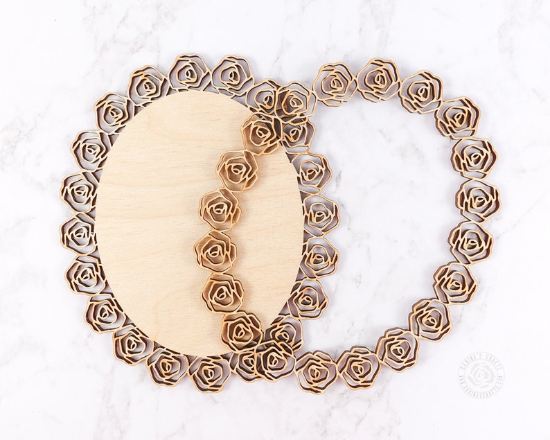 May include: Two wooden circular laser cut frames with a rose design. The frames are layered on top of each other, with the top frame slightly offset from the bottom frame.